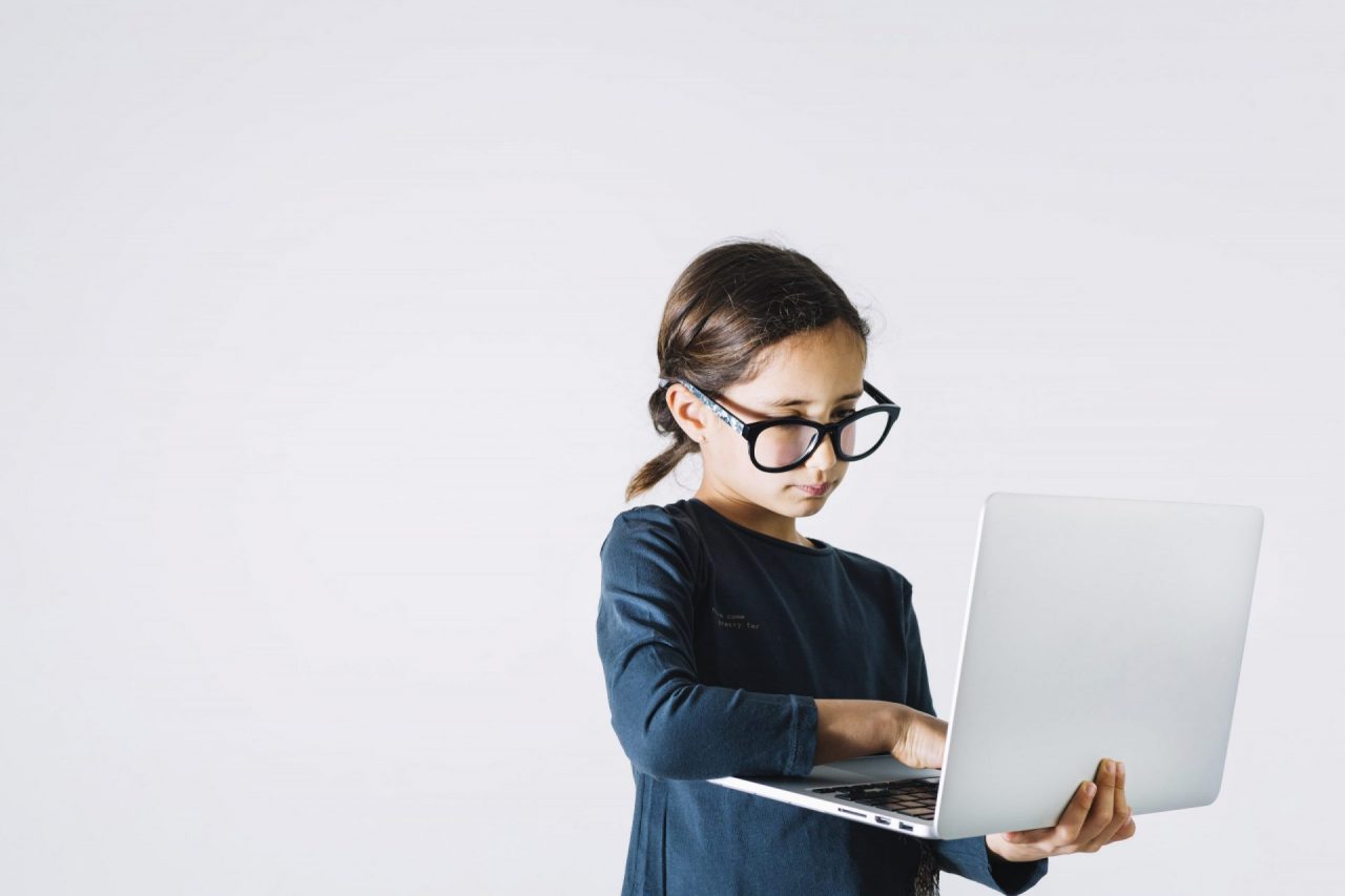 menininha de óculos, em pé, segurando computador