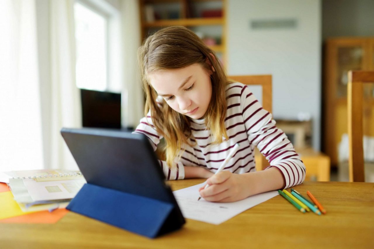 menina estudando, com auxilio de um tablet, papel e canetas